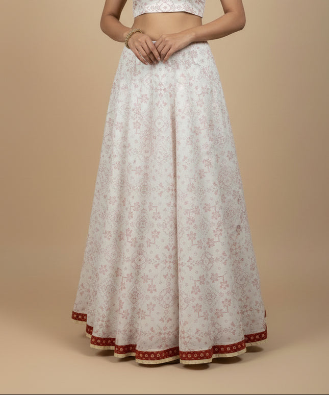 A long white A-line skirt with a pink geometric and floral pattern, displayed on a beige mannequin torso. The skirt features a red patterned hemband with gold trim.