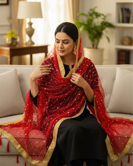 Kurti Connection USA red net dupatta with gold border, sequin embroidery, and tassels worn by a woman on a sofa.