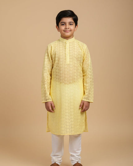 A young boy wearing a Kurti Connection USA yellow embroidered kurta with a mandarin collar and white churidar pants.